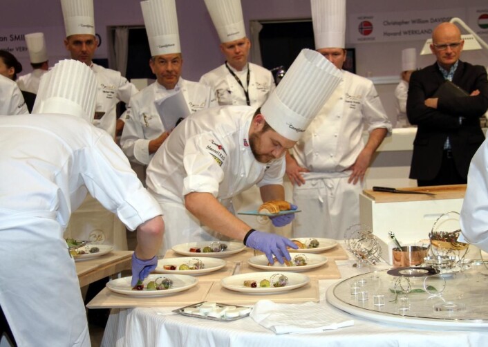 Christopher Davidsen gjør klar kyllingretten for juryen. To tidligere Bocuse d'Or-vinnere, Regis Marcon (1995) og Charles Tjessem (2003) følger med. Norges coach Gunnar Hvarnes skimtes rett bak Davidsen. (Foto: Morten Holt) Christopher Davidsen gjør klar kyllingretten for juryen. To tidligere Bocuse d'Or-vinnere, Regis Marcon (1995) og Charles Tjessem (2003) følger med. Norges coach Gunnar Hvarnes skimtes rett bak Davidsen. (Foto: Morten Holt)
