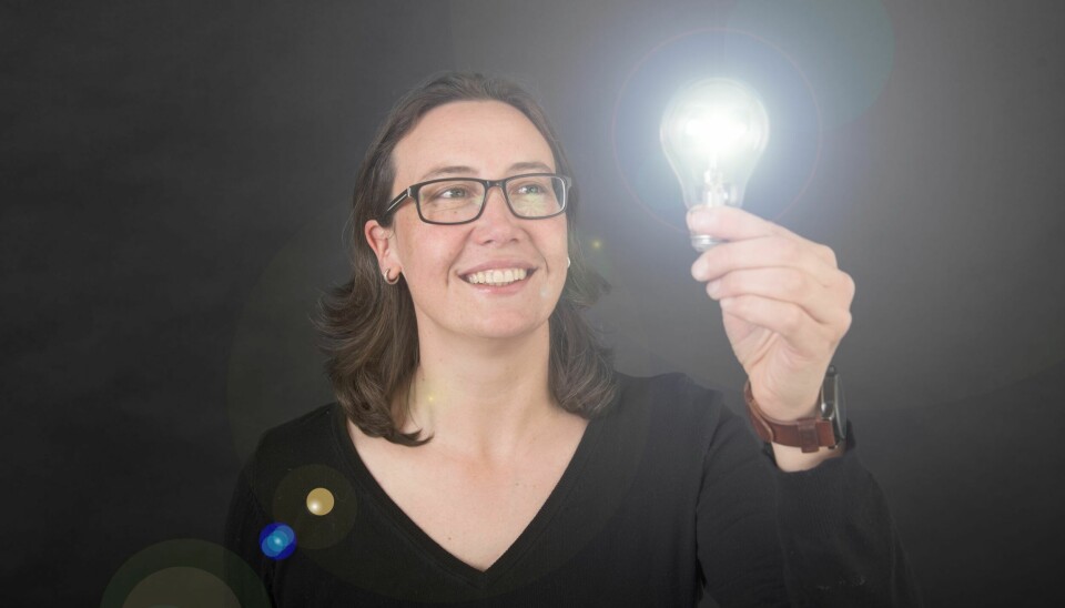 Seniorforsker Antje Gonera holder ei lyspære opp med venstre hånd. Mørkt hår og briller, mørk v-genser og mørk bakgrunn.